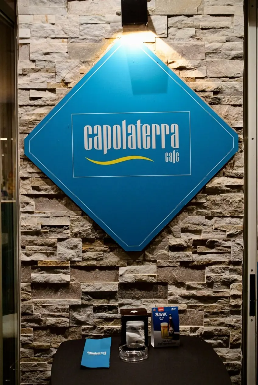 Insegna a diamante di Capolaterra Cafè illuminata sulla parete in pietra